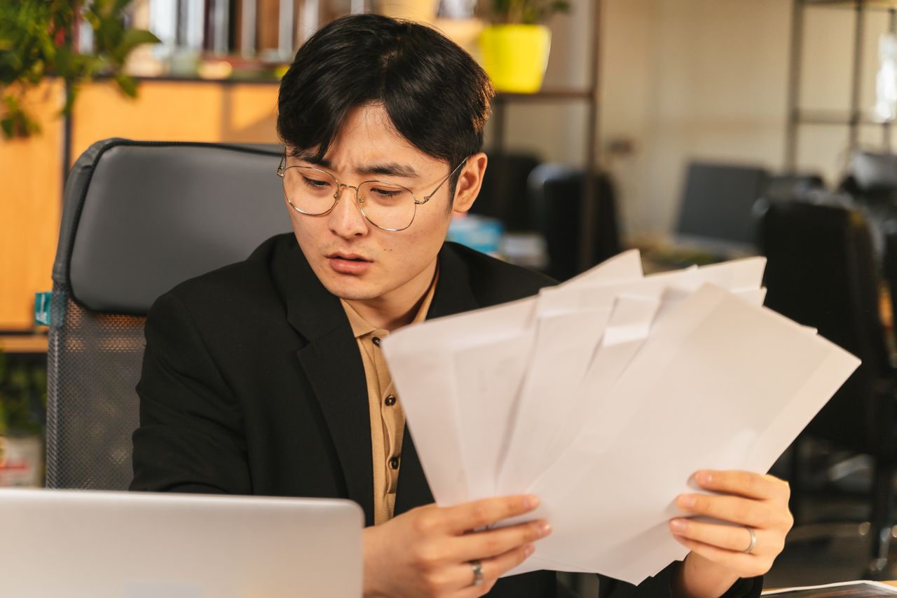 Businessman in glasses reviewing paperwork in a modern office setting.
